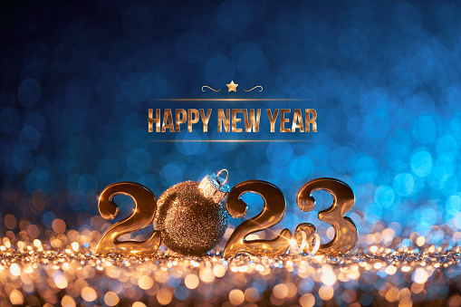 Abstract Christmas / New Year 2023 background. Golden serif numbers and a black glitter Christmas ornament on shiny stars, glitter and defocused lights in a yellow blue contrast. Native image size: 7952x5304