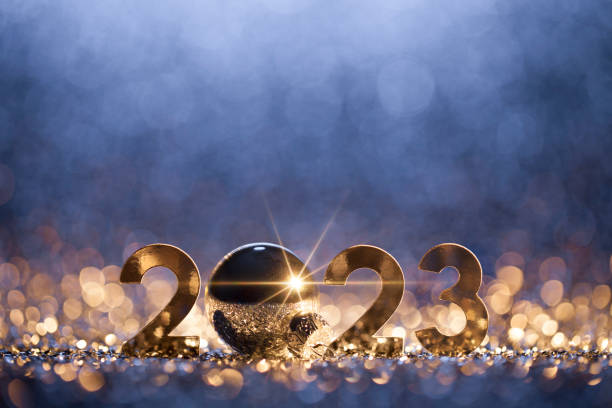Abstract Christmas / New Year 2023 background. Metallic numbers and a Christmas ornament on shiny stars, glitter and defocused lights in a yellow blue contrast. Native image size: 5616x3744