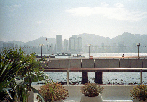 British Hong Kong, China - 1983: A vintage 1980's Fujifilm negative film scan of a photograph of the skyscrapers in downtown Hong Kong across the bay from waterfront balcony.