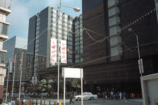 British Hong Kong, China - 1983: A vintage 1980's Fujifilm negative film scan of new office buildings and busy city streets in Hong Kong with pedestrians and cars.