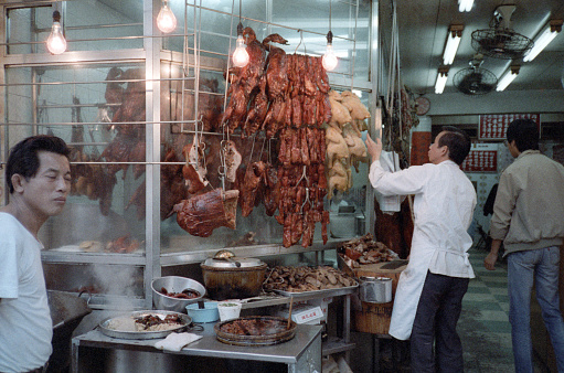 British Hong Kong, China - 1983: A vintage 1980's Fujifilm negative film scan of an open air meat market in downtown Hong Kong, with meat hanging and displayed.