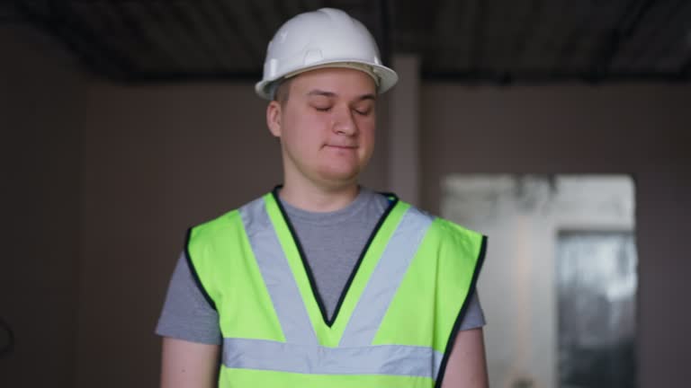 Overworking exhausted young builder yawning shaking hand leaving new apartment under construction. Portrait of tired Caucasian man walking away. Building and exhaustion.