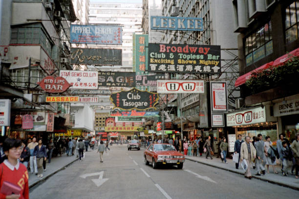 British Hong Kong, China - 1983: A vintage 1980's Fujifilm negative film scan of busy city streets covered in store signs in Hong Kong with pedestrians, cars, and shops.