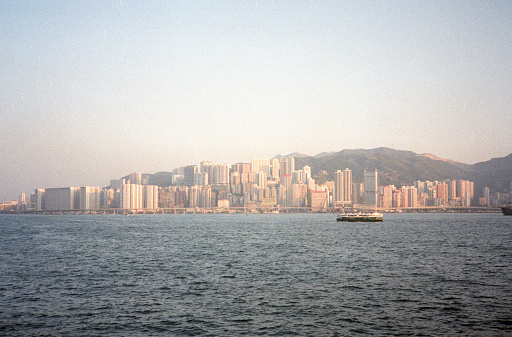 British Hong Kong, China - 1983: A vintage 1980's Fujifilm negative film scan of a photograph of the skyscrapers in downtown Hong Kong across the bay with sun starting to set.