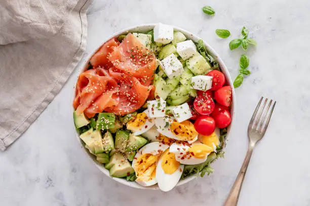 Overhead view of a low carb meal salad made of smoked salmon, hard boiled eggs, avocado, cucumber, tomatoes and leafy greens