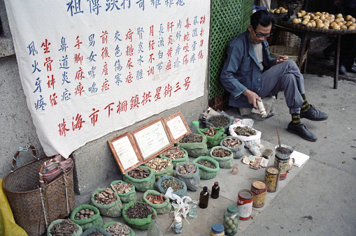 British Hong Kong, China - 1983: A vintage 1980's Fujifilm negative film scan of spice street market vendor in downtown Hong Kong, with spices on display in front of a sign.
