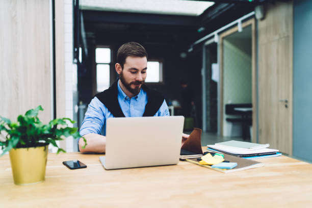 istock Cheerful business man with laptop sitting at table and using notebook 1417387507