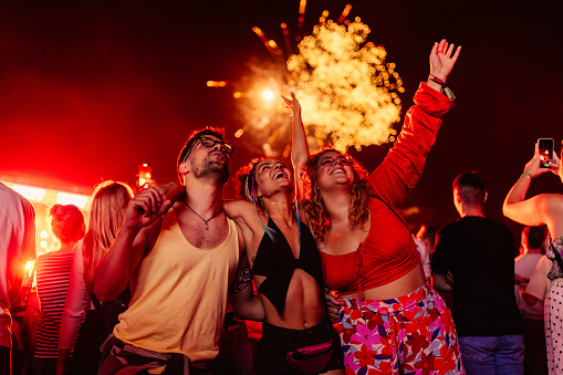 A group of casual young friends are enjoying the fireworks display in the night sky at a festival