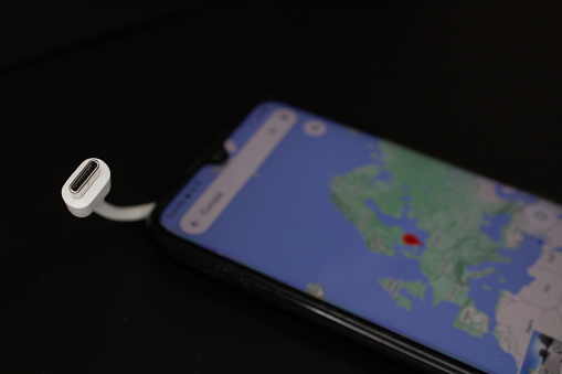 Charging cable plug for type C charging port, next to a smartphone showing a map of Europe, on a black background