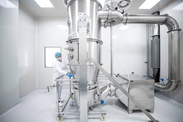 Woman wearing protective wear seen working on the machine in a laboratory during pharmaceutical manufacturing Female employee in a pharmaceutical factory wearing protective gloves, mask, cap and suit in a laboratory seen working on a specific machine that is the part of the medicaments production during the working hours. pharmaceutical factory stock pictures, royalty-free photos & images