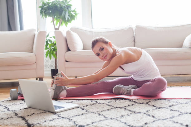 istock Attractive sportswoman with laptop doing exercise at home. 1417394418