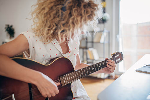 One woman, mature female with headphones sitting at the desk in bedroom at home, she is playing acoustic guitar.