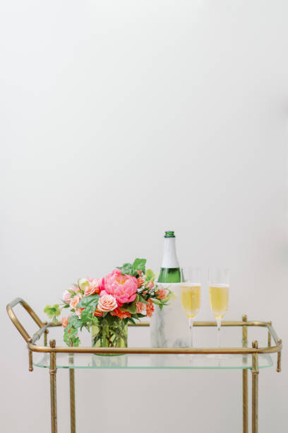 pink and peach flowers on bar cart with champagne and two glasses stock photo