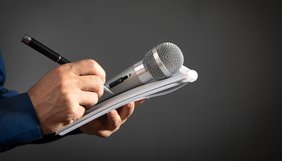 Caucasian journalist holding microphone, notepad and pen.