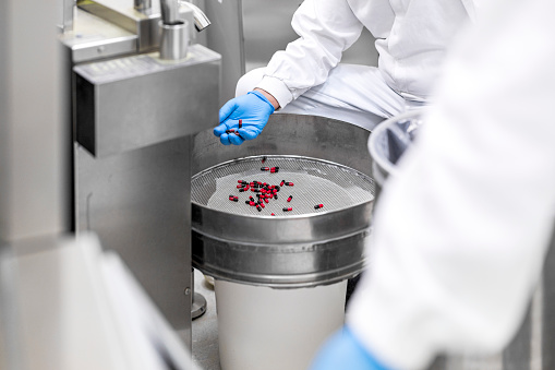 Pharmaceutical technician's hands seen in a special laboratory while holding and controlling red and black pills during usual procedure after production of the drugs.