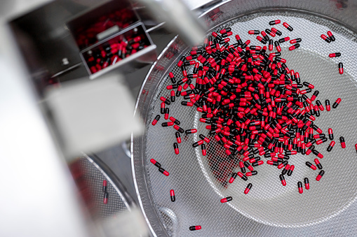 Close up on a big industrial sieve with red and black pills in it seen during usual procedure after production of the drugs in a pharmaceutical factory.