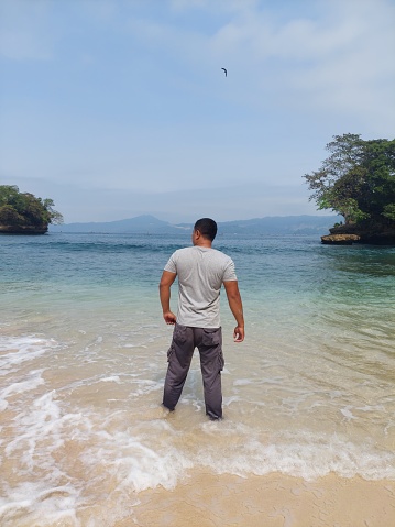 Full length view of an Indonesian young man standing at the beach overlooking to the sea