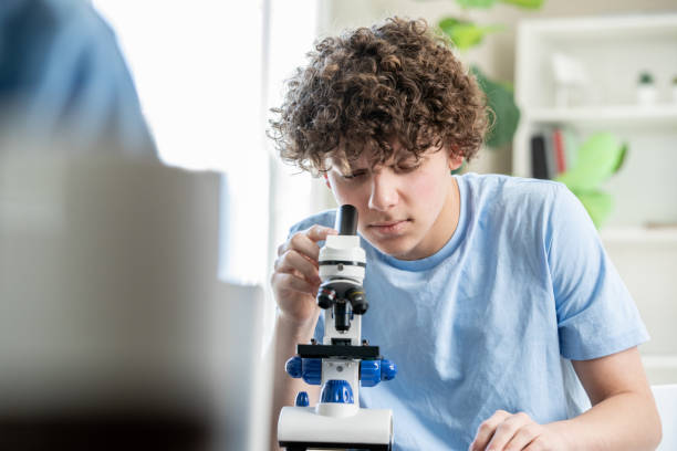 estudante do ensino médio olhando através de um microscópio na aula de ciências. - science child laboratory education - fotografias e filmes do acervo