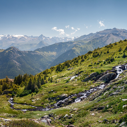 Landscape of Oisans massif in summer with a flowing water stream. This image was taken near Ornon small village in Alps mountains, in Isere, Auvergne-Rhone-Alpes region in France.