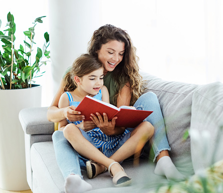 Mother and daughter reading a book on sofa at home
