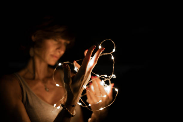 istock Woman, blurred face, holding string lights in the dark. Copy space. 1417418192