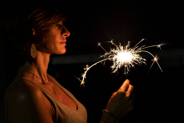 Woman, side view, holding a burning sparkler in the dark. stock photo