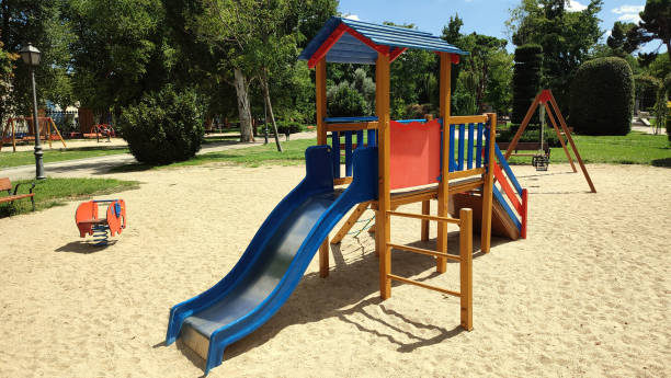 istock empty playground with swing, slide and attractions for children, on a sandy ground and a park with trees around on a sunny day 1417420094
