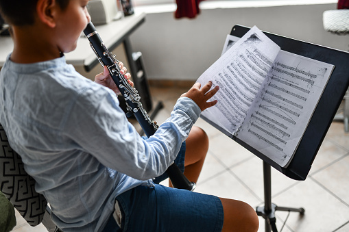 Male Child Turning Page On Exercise Sheet Music Book While Practicing Clarinet