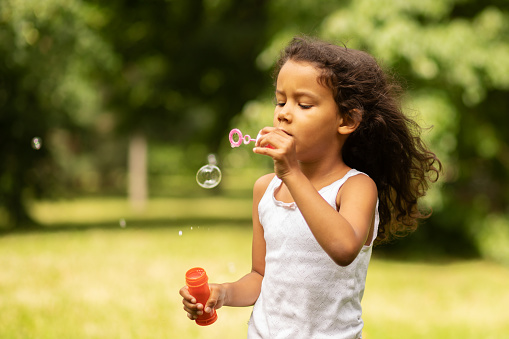 happy african american child outdoor, girl blowing bubbles