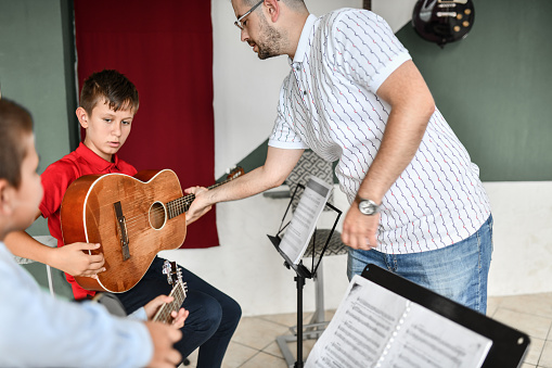 Guitar Teacher Showing Boys How To Hold Guitar