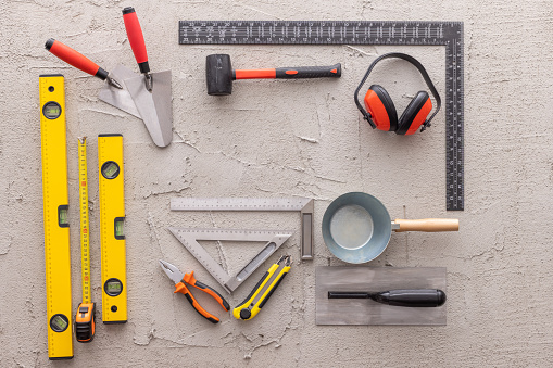 Various construction, DIY hand tools on a concrete background. Tools include: hammer, level, tape measure, masonry equipment, scalpel,  pliers and nippers