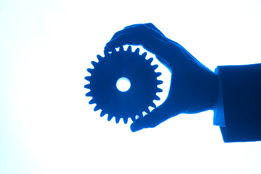 One hand holding a gear against a white background. Silhouette.