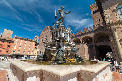 Bologna, Italy - August 21, 2022: street view of the Fondana di Nettuno in Bologna, people are visible in the far distance under a blue sky of summer.