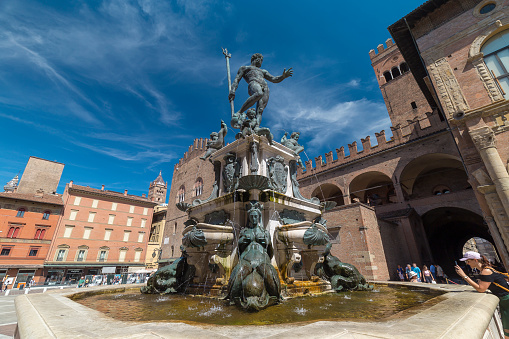 Bologna, Italy - August 21, 2022: street view of the Fondana di Nettuno in Bologna, people are visible in the far distance under a blue sky of summer.