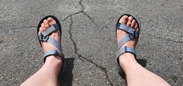 Legs of a man in summer shoes against the background of cracked asphalt. Elegant men's open shoes