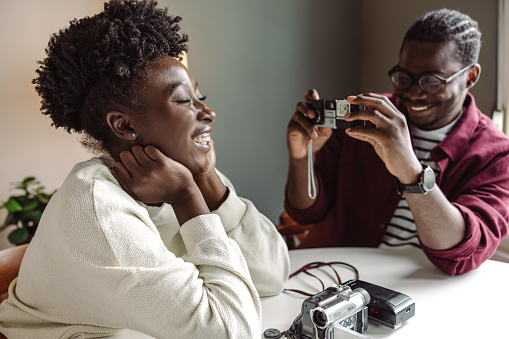 Shot of African-American young couple at the table, they are playing with vintage and analog cameras