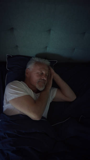 Mature man relaxing in comfortable bed. Smiling and feeling cozy afetr fighting insomnia stock photo
