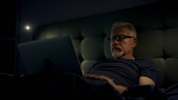 istock Mature man in bed can't sleep due to insomnia. Using laptop 1417450678