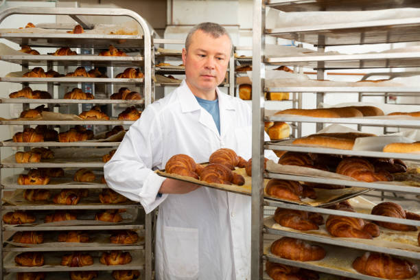 istock Baker placing tray with baked rolls on trolley 1417458408