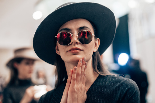 Female portrait of beautiful woman who working fashion model at the fashion week show. Backstage photography, behind the scenes of new clothing collection. Girl wear eyeglasses and hat.