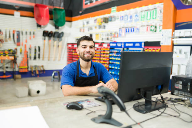 Happy hardware store employee at the computer desk at work Attractive cashier and store worker sitting at the computer desk and ready to help a client or give customer service hardware store stock pictures, royalty-free photos & images