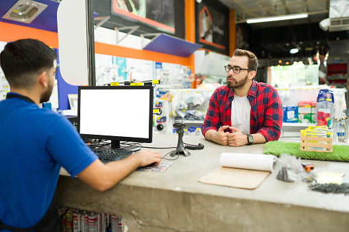 Attractive young man and customer waiting for a hardware store worker to pay for his power and construction tools