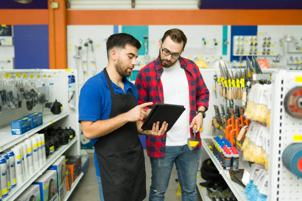 dipendente attraente alla ricerca di un prodotto con un cliente presso il negozio di ferramenta - hardware store store work tool customer foto e immagini stock