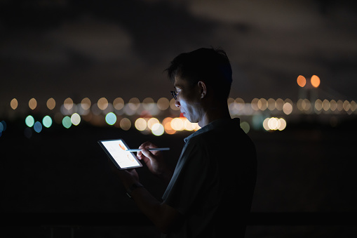 man using tablet by the sea at night