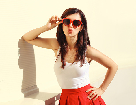 Portrait of beautiful young brunette woman wearing red heart shaped sunglasses posing in the city