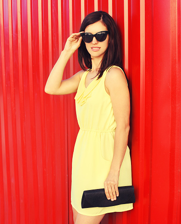 Portrait of beautiful brunette young woman wearing yellow dress, handbag clutch on red background