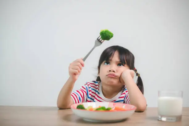 Photo of Nutrition & healthy eating habits for kids concept. Children do not like to eat vegetables. Little cute girl refuses to eat healthy vegetables.