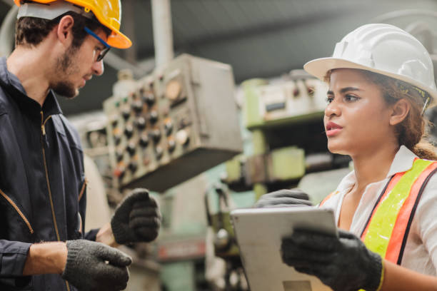 istock Female industrial engineer wearing a white helmet while standing in a heavy industrial factory behind she talking with workers, Various metal parts of the project 1417486782