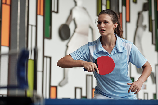 Determined young woman playing table tennis in gym