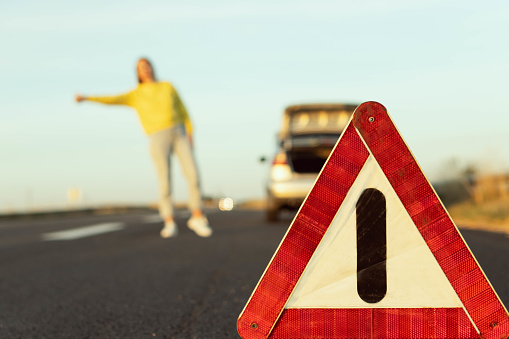 in the foreground, an emergency stop sign in focus, in the background, a blurred girl in a yellow jacket stands with her hand raised, stops the car for roadside assistance